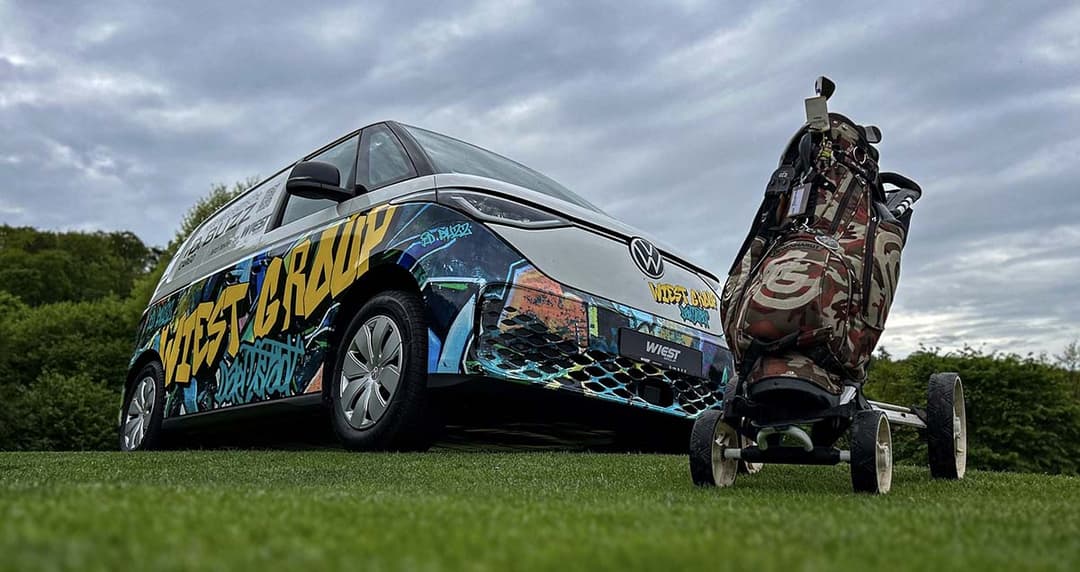 Folierter ID.Buzz auf einer grünen Wiese hinter einem Golftrolly