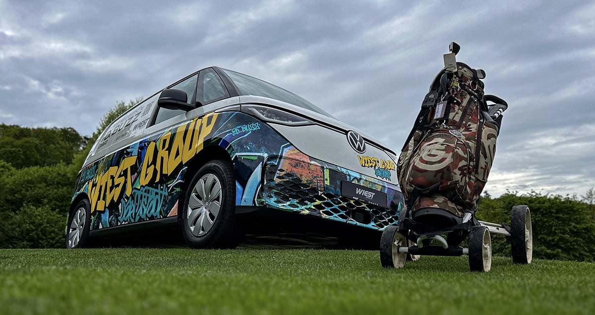 Folierter ID.Buzz auf einer grünen Wiese hinter einem Golftrolly